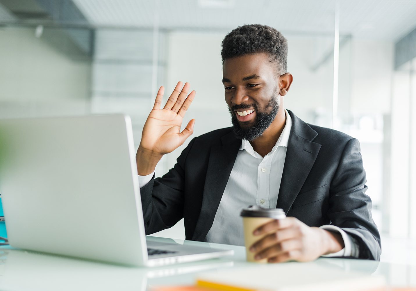 Young African manager with stubble sitting in front of open laptop wearing earphones while having video conference call with business partners